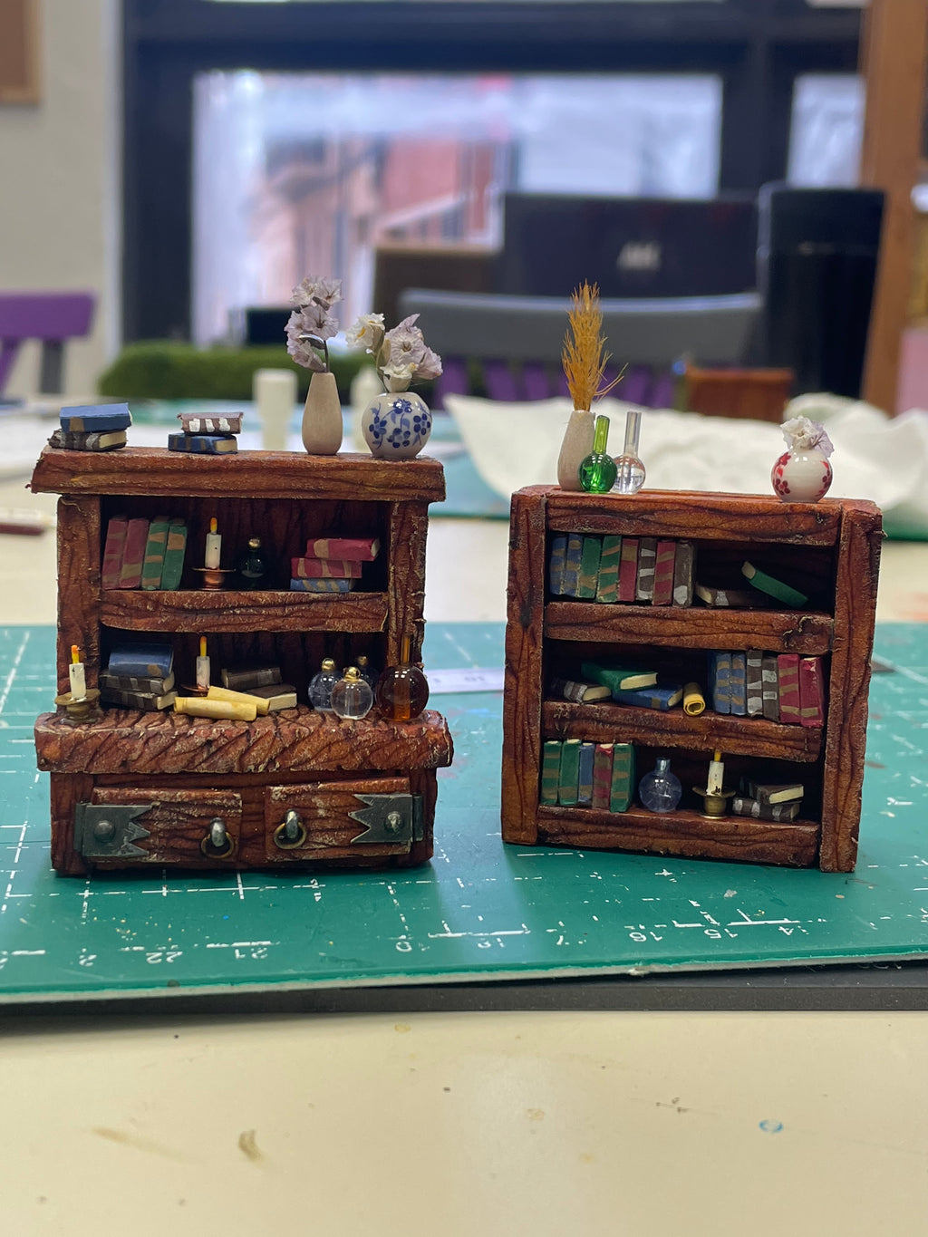Dos librerías de madera en miniatura con libros, cajones y recipientes decorativos