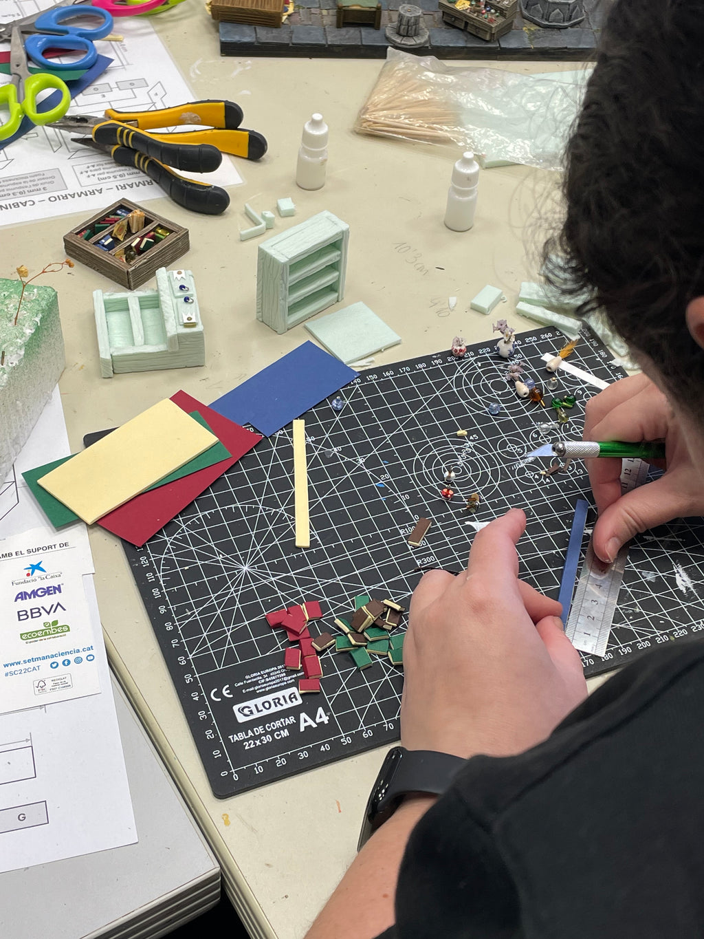 Manos trabajando en pequeñas piezas de mobiliario sobre una base de corte