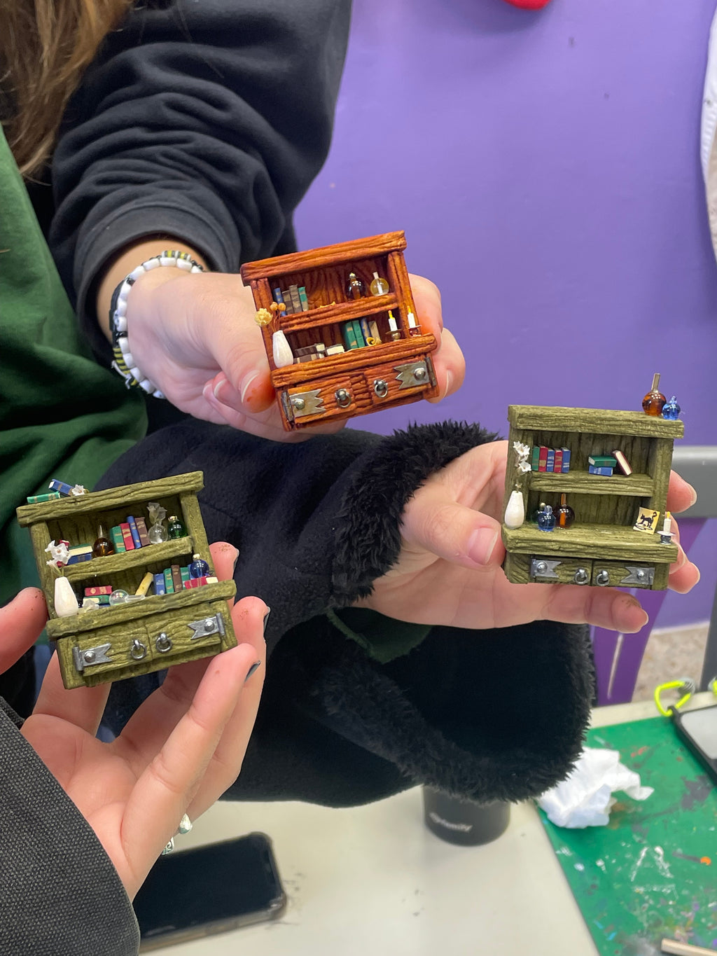 Tres librerías en miniatura terminadas, sostenidas por participantes del taller