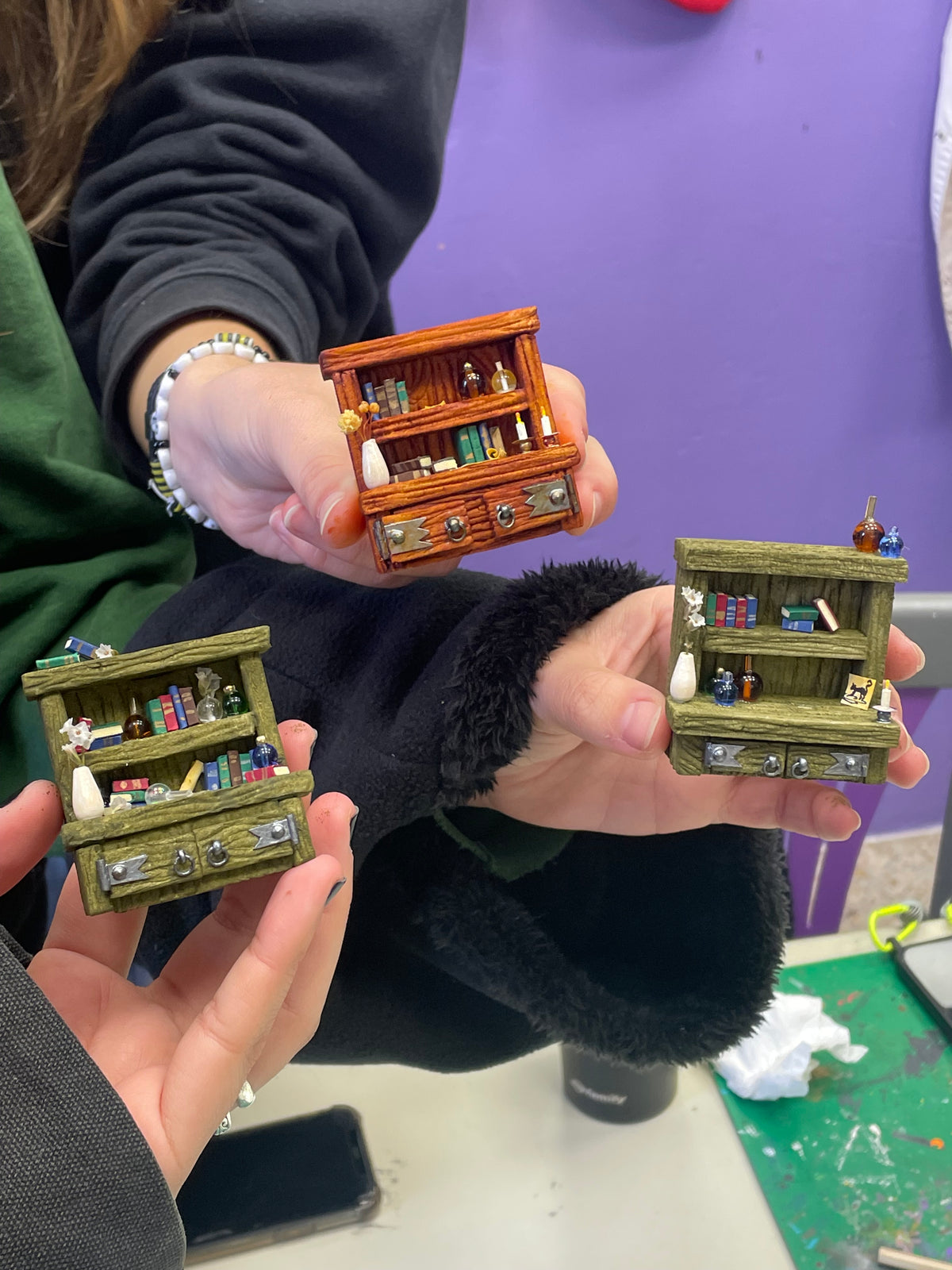 Tres librerías en miniatura terminadas, sostenidas por participantes del taller
