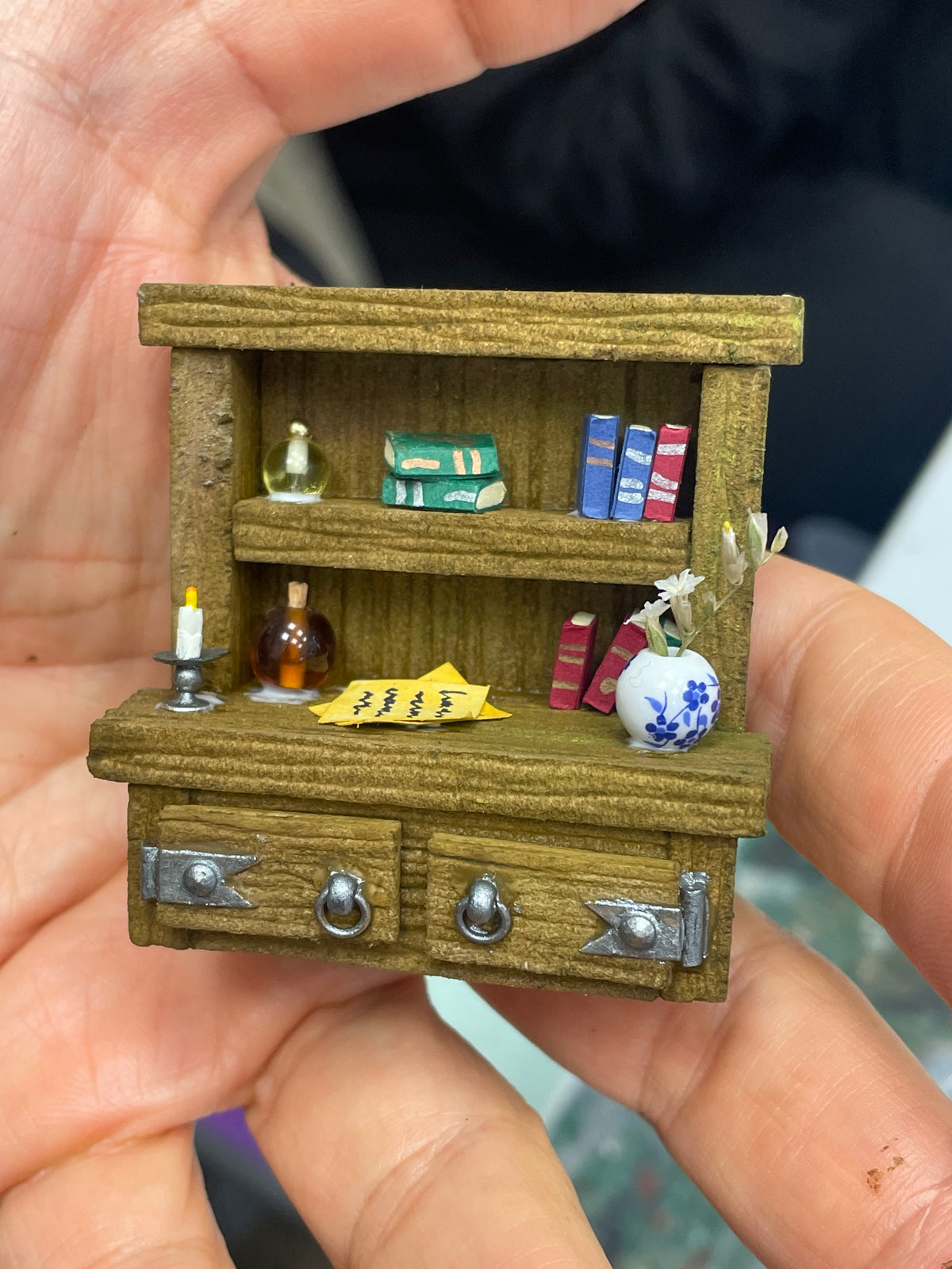 Detalle de una librería verde y dorada en miniatura con libros, frascos y cajones